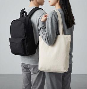 A person wearing a backpack and holding a canvas tote bag.